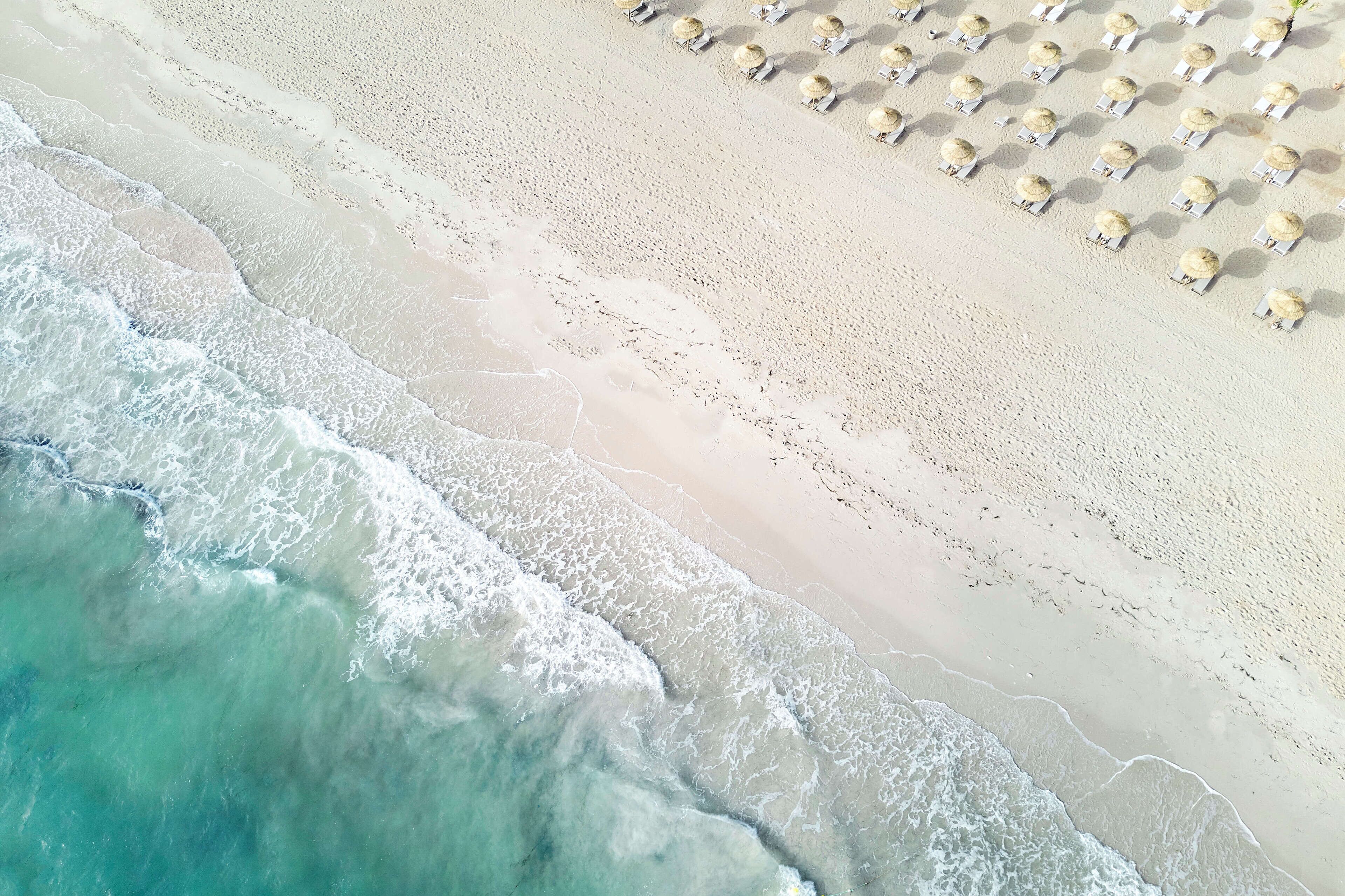 An aerial view of a beach with rows of sun loungers and umbrellas.