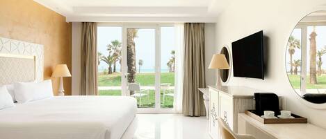 A hotel room with a large bed, a desk with a TV, and a view of the beach.