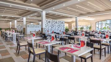 A spacious dining area with multiple tables and chairs, a modern ceiling design, and large windows allowing natural light.
