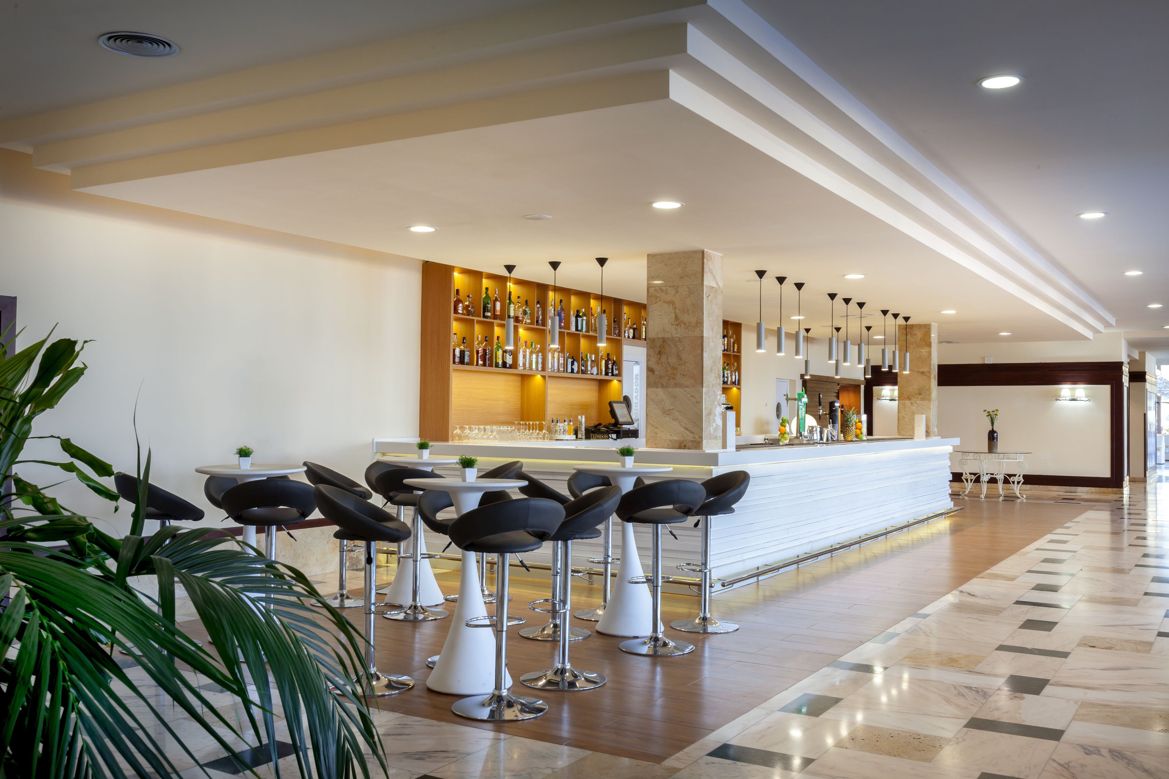 A modern bar area with a marble countertop, multiple bar stools, and a variety of bottles and glasses.