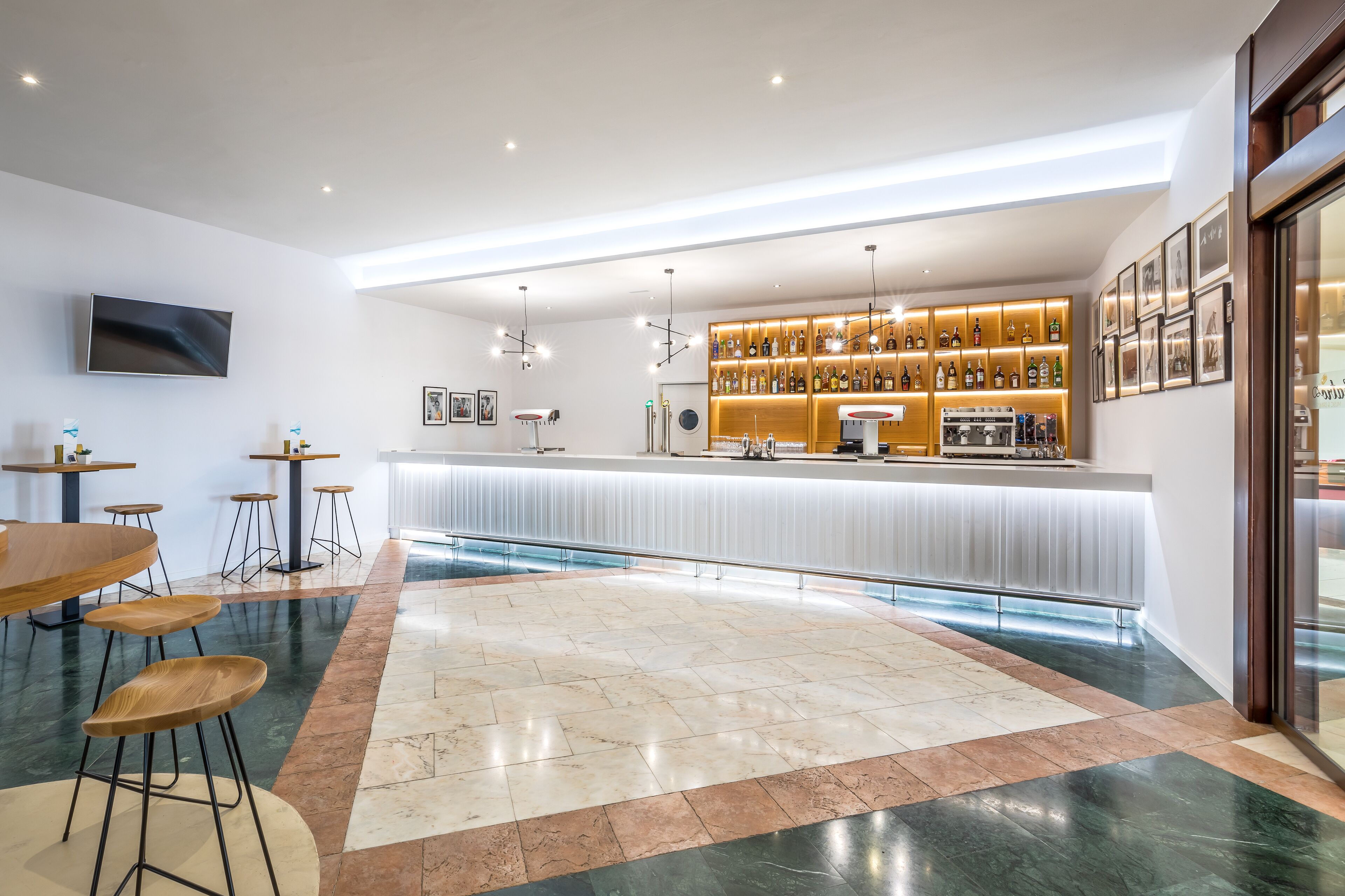 Zona de bar moderna con una barra larga, taburetes y una variedad de botellas.
