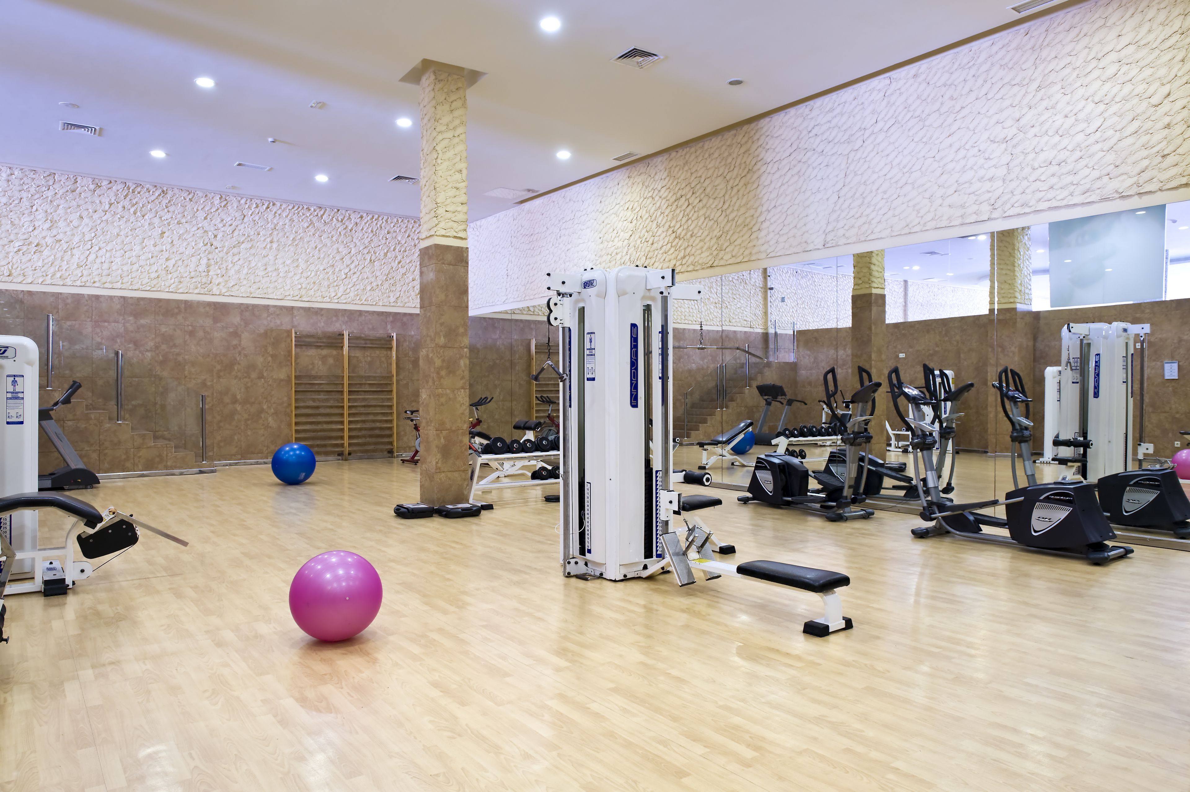 A gym with various exercise equipment, a large mirror, and a wooden floor.