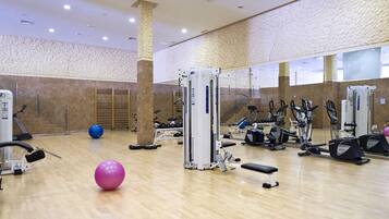 Un gimnasio con diversos equipos de ejercicio, un espejo grande y suelo de madera.