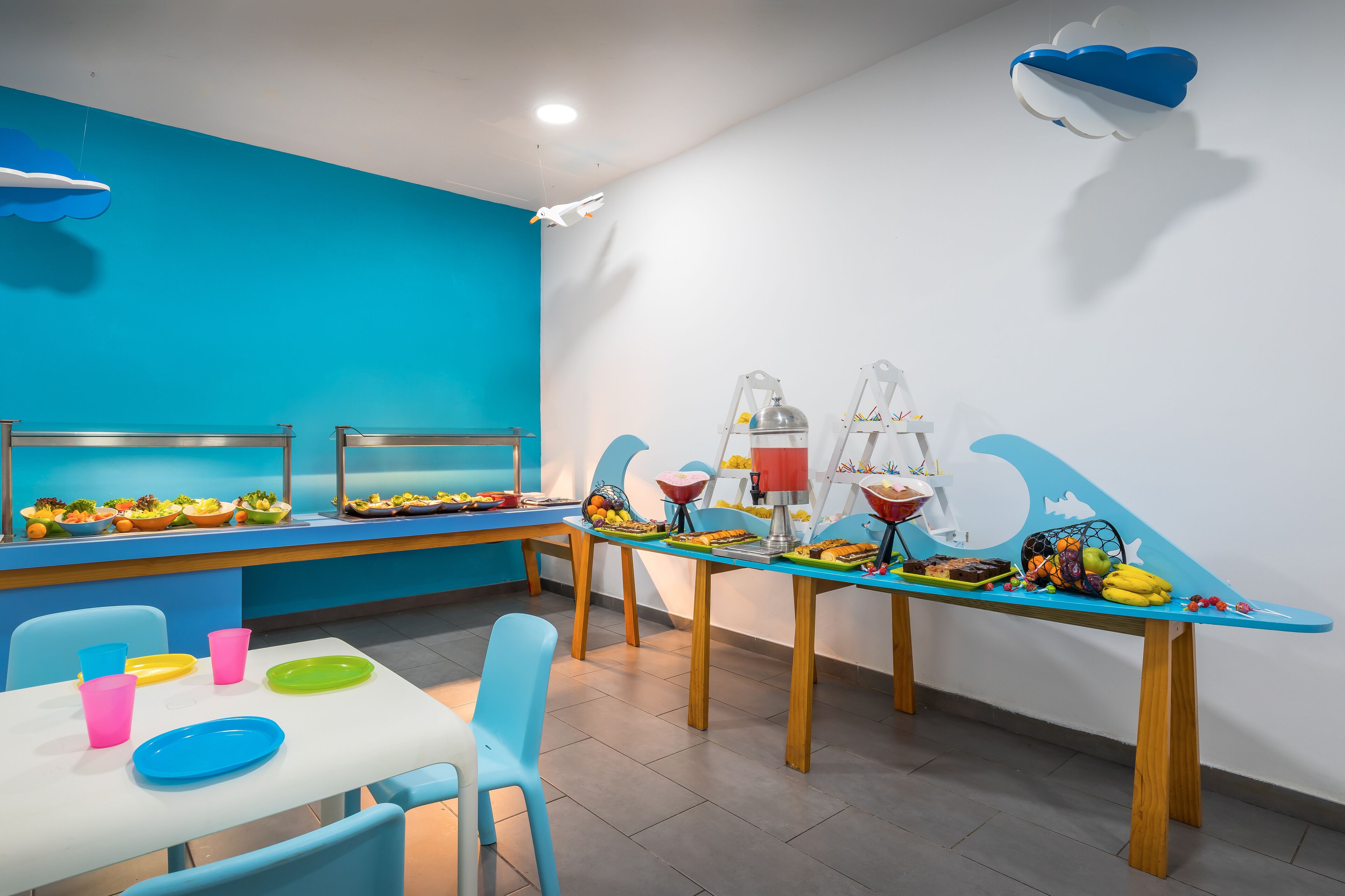Une salle à manger aux couleurs vives, avec des tables dressées pour le repas, où l’on peut admirer une variété de plats et une vaisselle colorée.