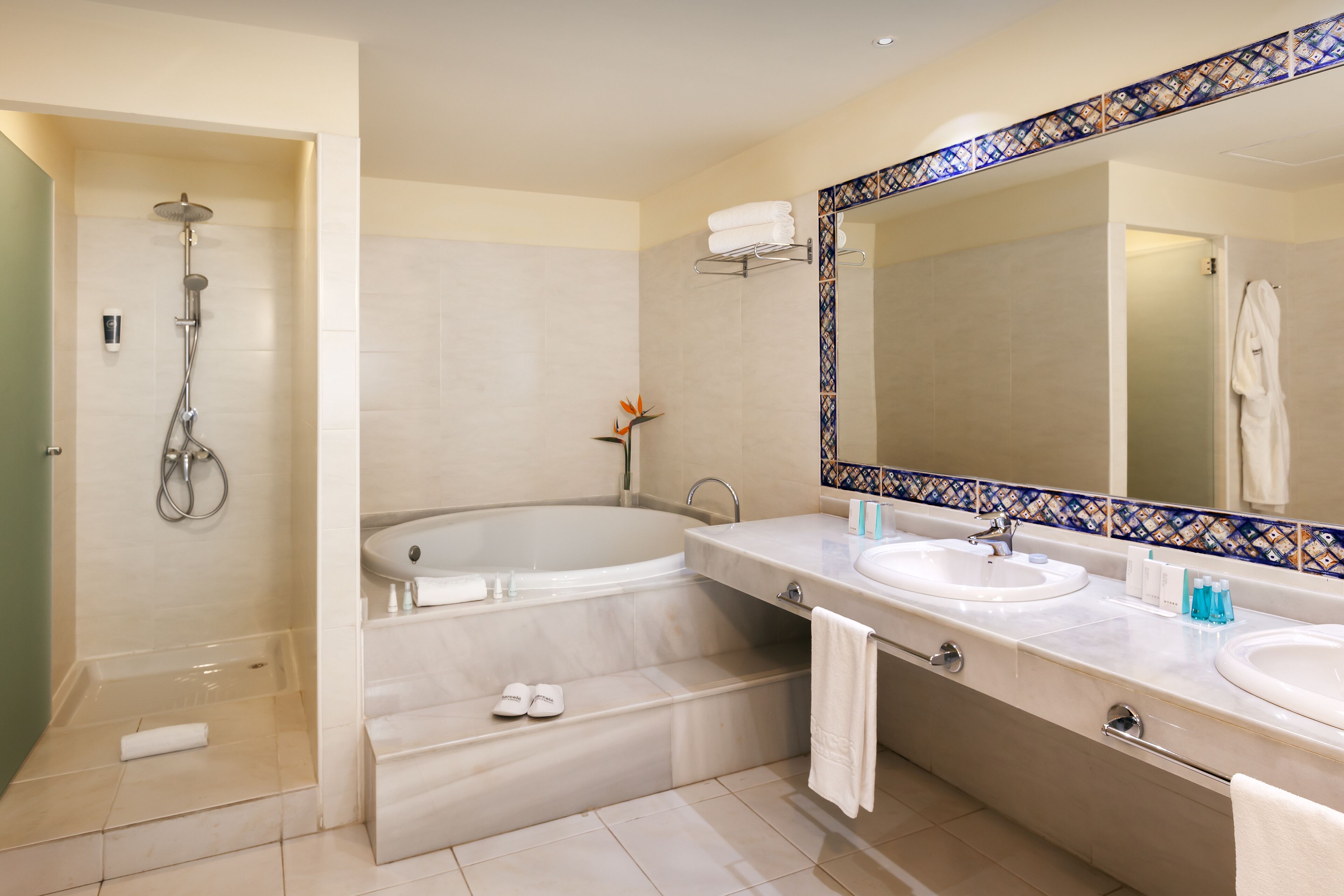 A bathroom with a bathtub, two sinks, a shower, and a mirror with a decorative tile border.