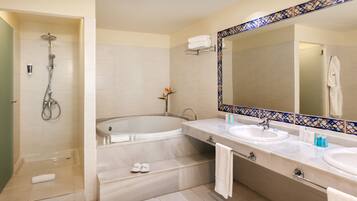 A bathroom with a bathtub, two sinks, a shower, and a mirror with a decorative tile border.