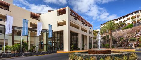 A hotel with a modern facade, large windows, and a landscaped area with a fountain.