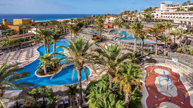 A resort with multiple swimming pools, palm trees, and a view of the ocean. - Occidental Jandía Mar - All Inclusive (Pajara)