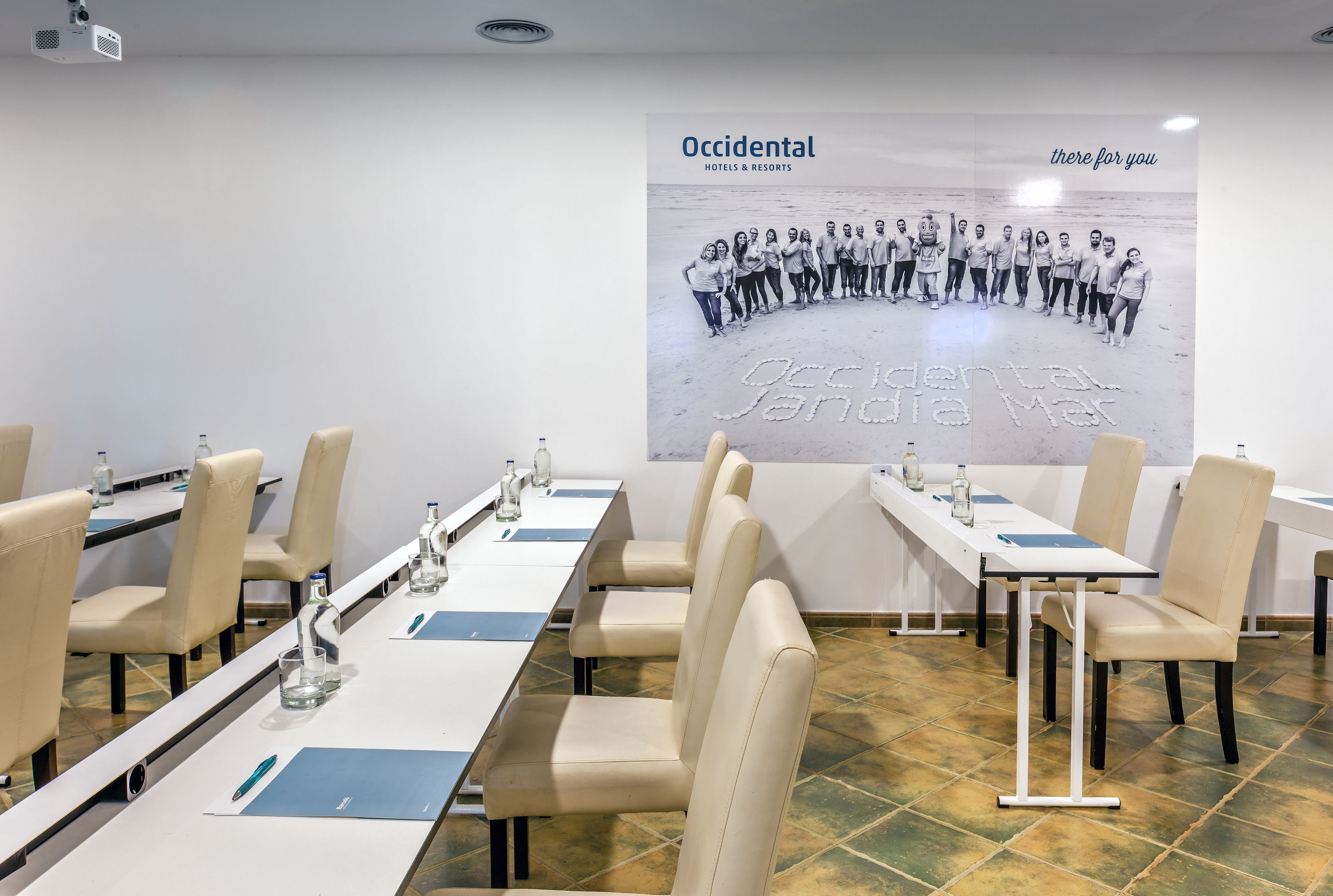 Ein Konferenzraum mit langen Tischen, Stühlen und einer Projektionsleinwand.