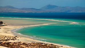 A coastal landscape with a wide sandy beach, clear turquoise waters, and distant mountains. - Occidental Jandía Mar - All Inclusive (Pajara)
