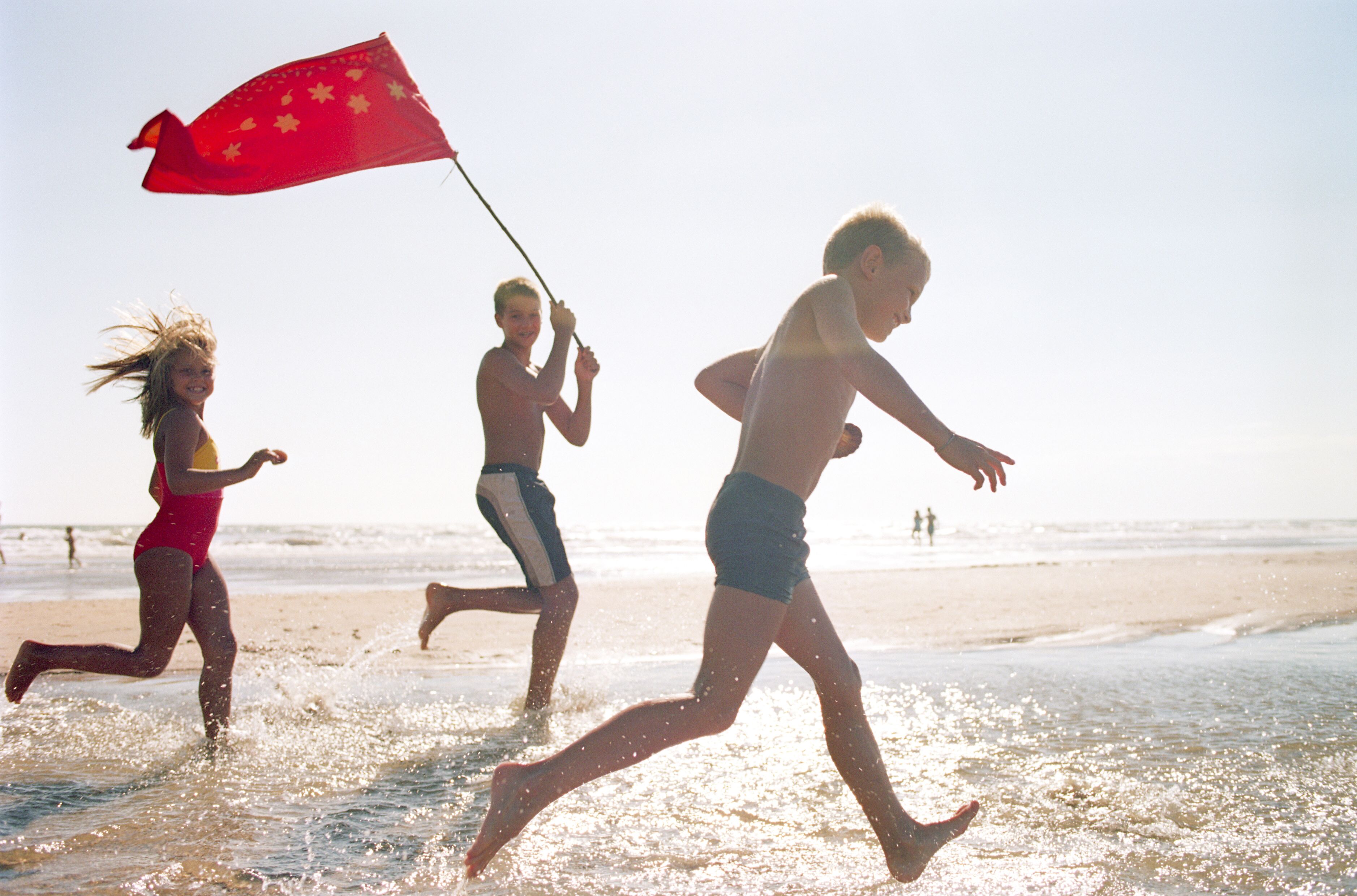 Tres personas corriendo en una playa con una bandera.