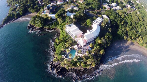 An aerial view of a resort island with a large building, a swimming pool, and lush vegetation. - Blue Haven Hotel (Scarborough)