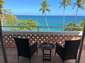 A balcony with wicker chairs and a small table, overlooking a coastal view with palm trees and the ocean. - Blue Haven Hotel (Scarborough)