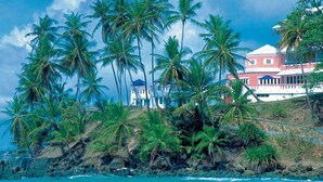 A coastal property with a prominent red building, lush palm trees, and a rocky shoreline. - Blue Haven Hotel (Scarborough)