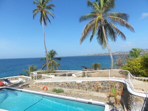 A pool area with a view of the ocean, palm trees, and a stone wall. - Blue Haven Hotel (Scarborough)
