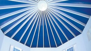 A spacious room with a high ceiling and a radial design. There is a dining table with chairs and a flower arrangement in the center. - Blue Haven Hotel (Scarborough)