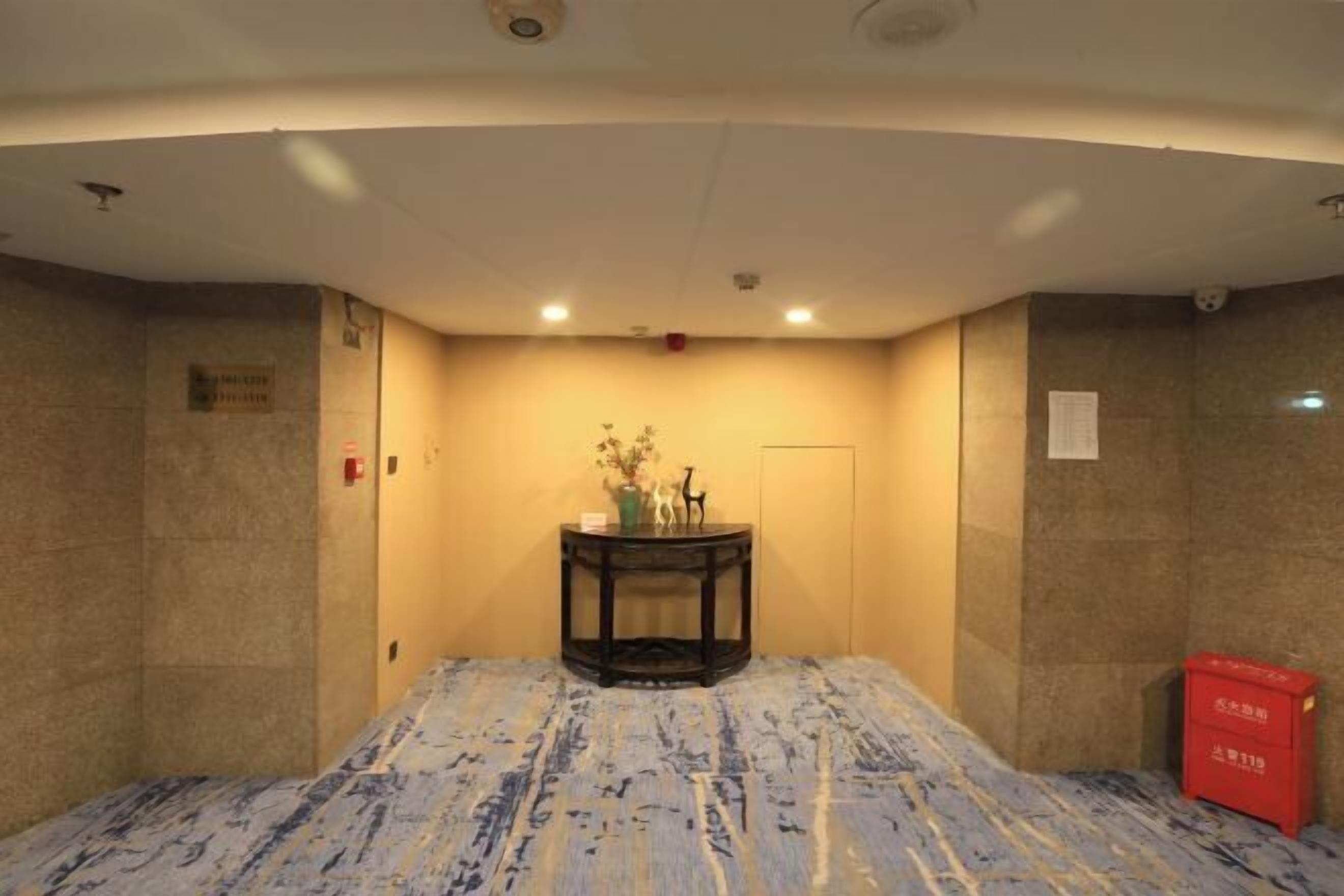 A hotel room with a marble-patterned floor, a small table with a vase and figurines, and a red box on the right.