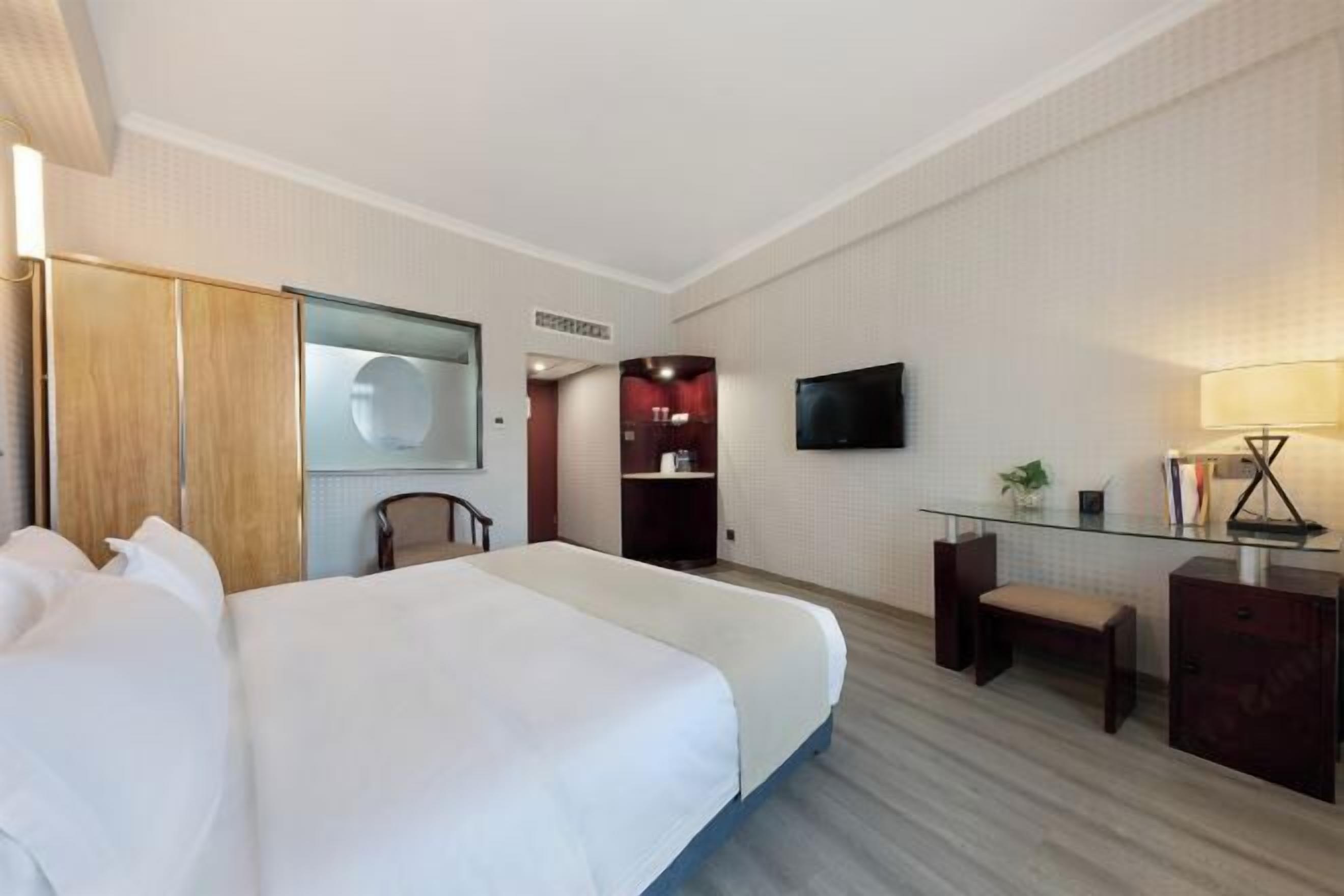 A hotel room with a large bed, a desk with a chair, a TV, and a small seating area.