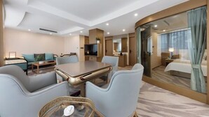 A hotel room with a dining area, a TV, a bed, and a bathroom with a glass shower. - Chengdu Pearl International Hotel (Chengdu)