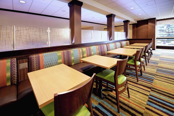 A restaurant with booth seating and individual tables, featuring a patterned carpet and wooden furniture. - Fairfield Inn & Suites by Marriott Wausau (Schofield)