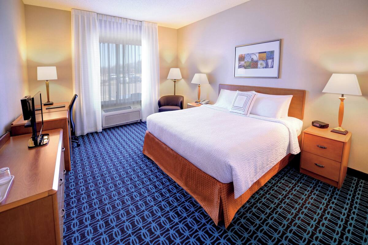 Une chambre d’hôtel avec un grand lit, deux tables de chevet avec des lampes, un bureau avec une chaise et une fenêtre avec des rideaux.