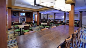 A spacious dining area with multiple tables and chairs, a television in the background, and a patterned carpet. - Fairfield Inn & Suites by Marriott Wausau (Schofield)