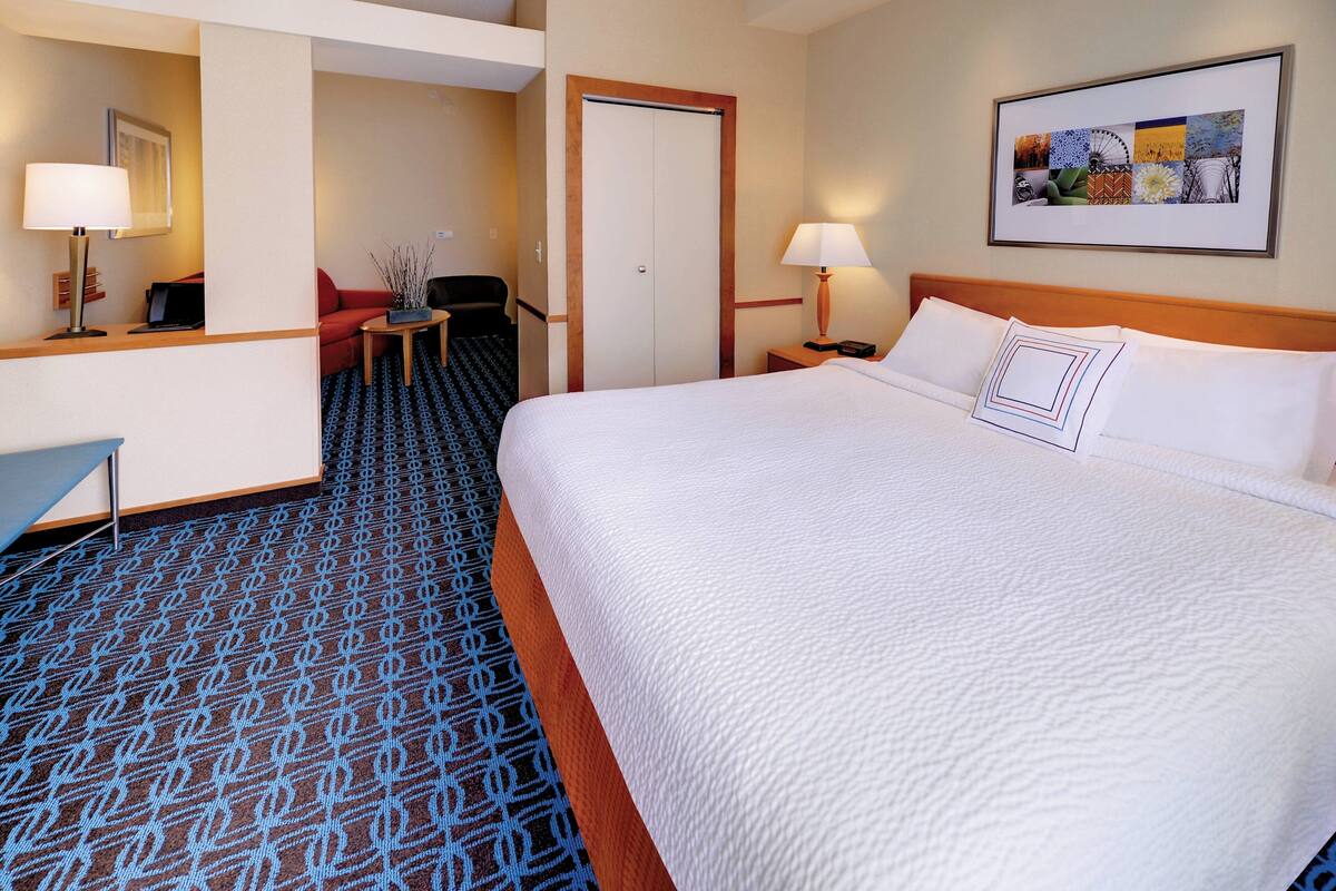 Une chambre d’hôtel avec un grand lit, un bureau avec une lampe, une chaise et une porte.