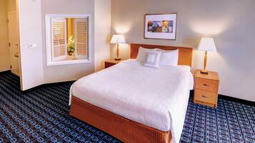A hotel room with a large bed, two bedside tables with lamps, a window with blinds, a framed picture on the wall, and a patterned carpet.