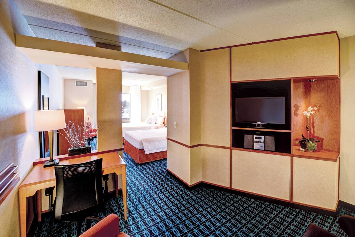 Une chambre d’hôtel comprenant un lit, un bureau avec une chaise, une télévision et une petite étagère ornée d’objets décoratifs.