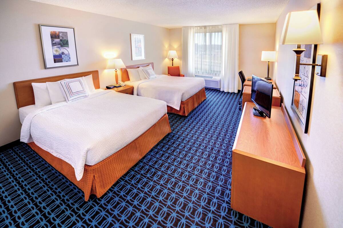 Une chambre d’hôtel avec deux lits, un bureau avec un ordinateur et une grande fenêtre avec des rideaux.