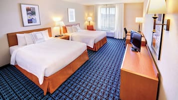 Een hotelkamer met twee bedden, een bureau met een computer en een groot raam met gordijnen.