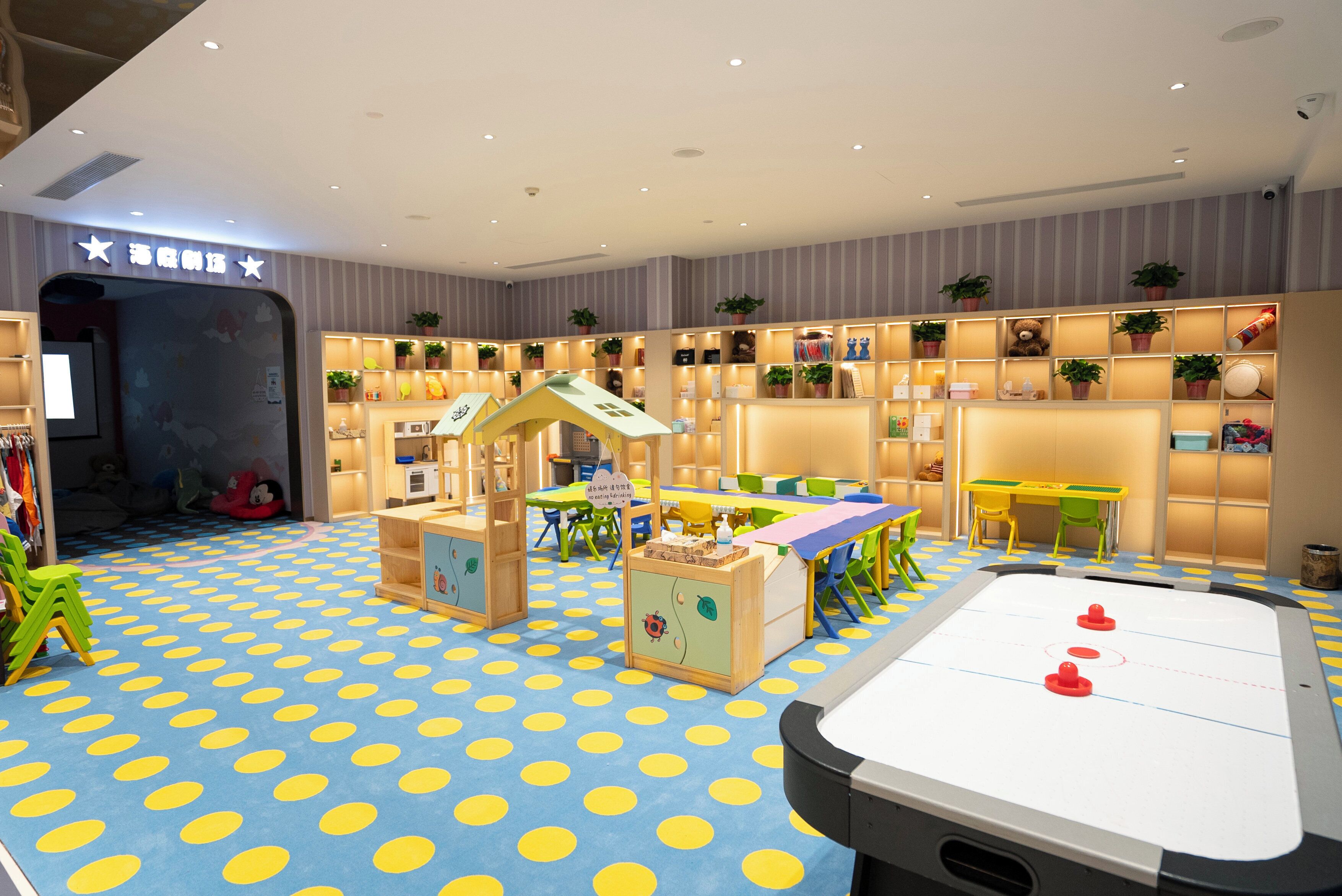 A children's play area with a blue polka dot floor, a small playhouse, and a foosball table.