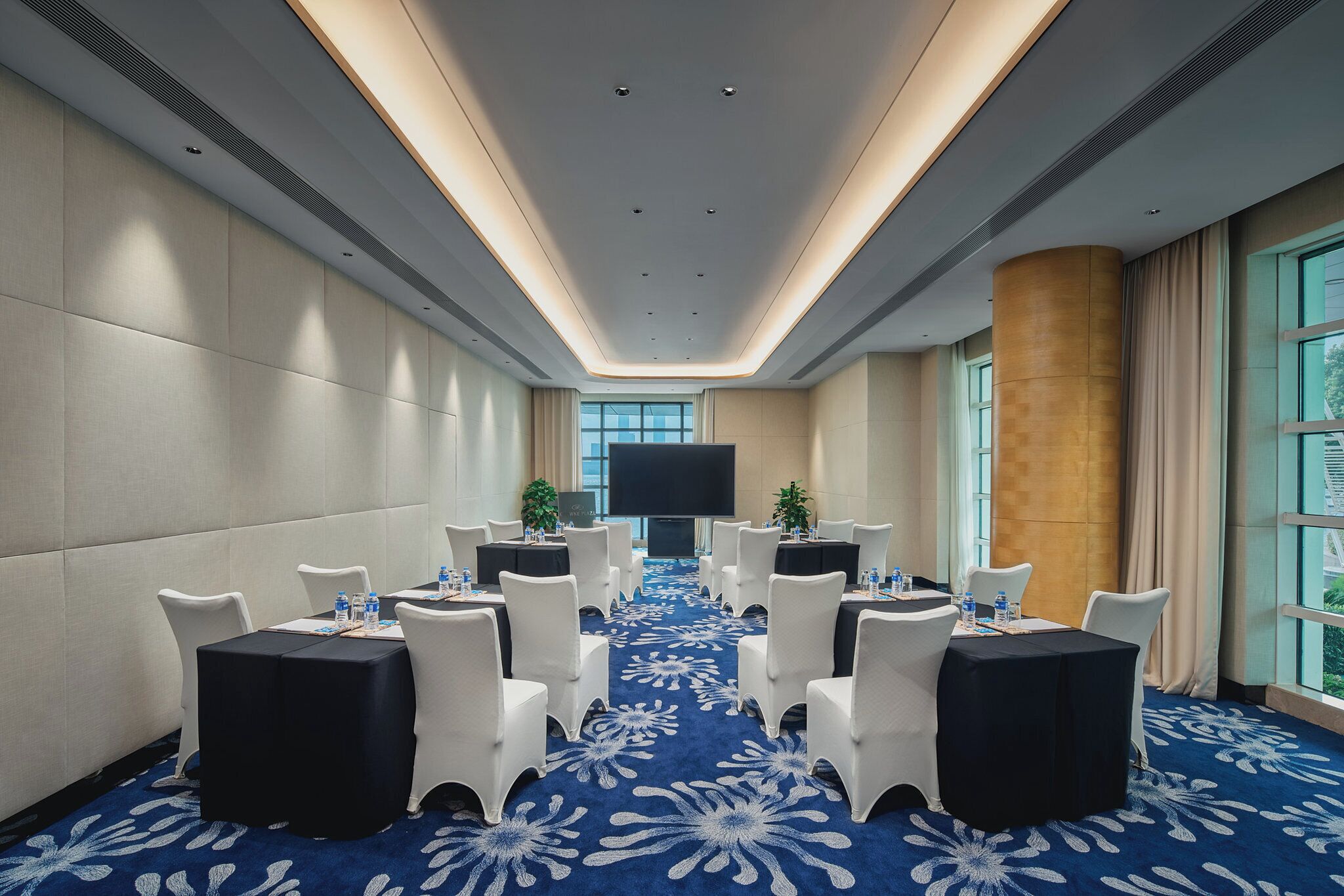 Un salón de conferencias con mesas redondas, sillas blancas y alfombra azul.