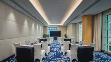 Un salón de conferencias con mesas redondas, sillas blancas y alfombra azul.