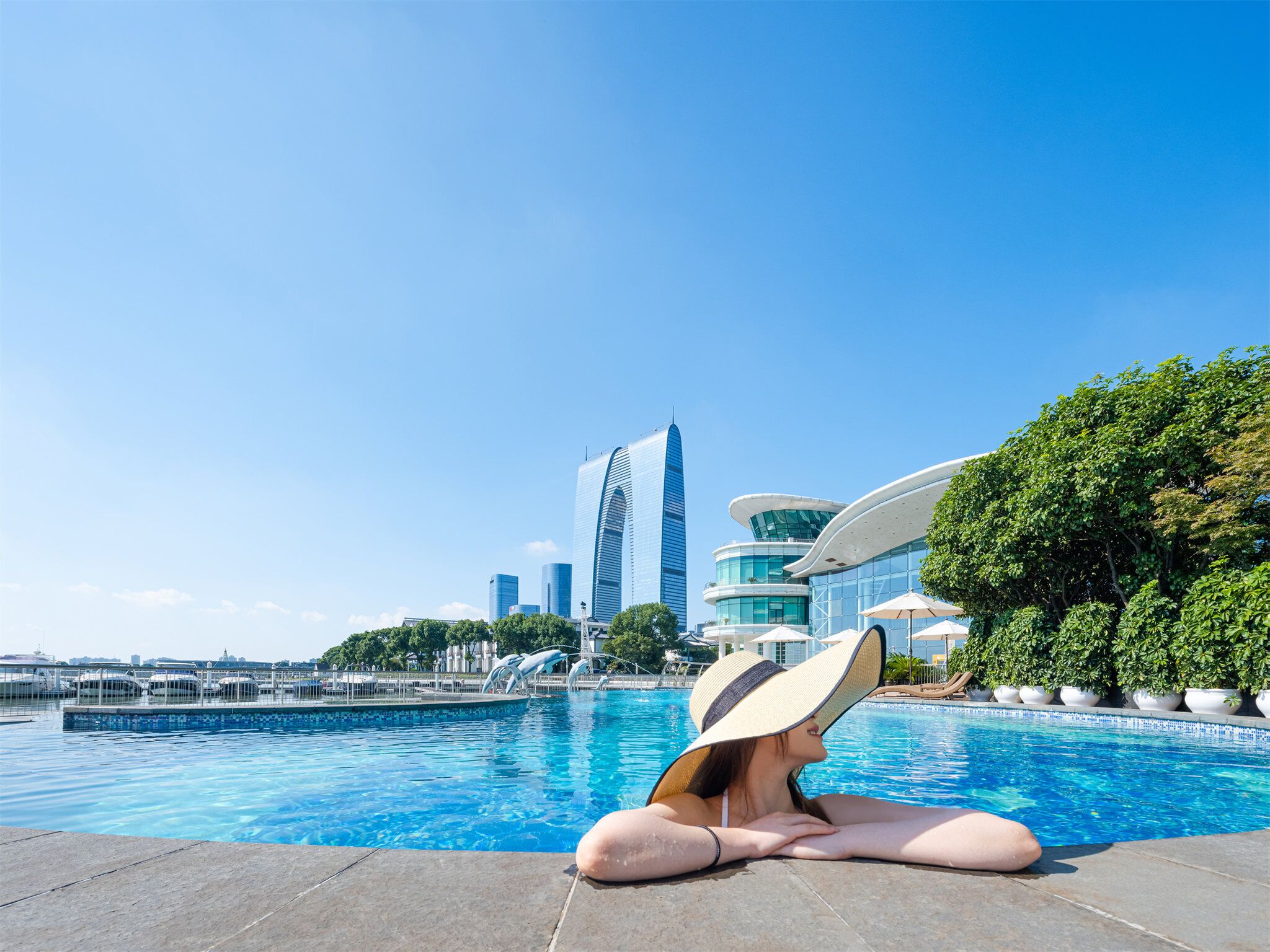 A woman relaxing by a swimming pool with a cityscape in the background.