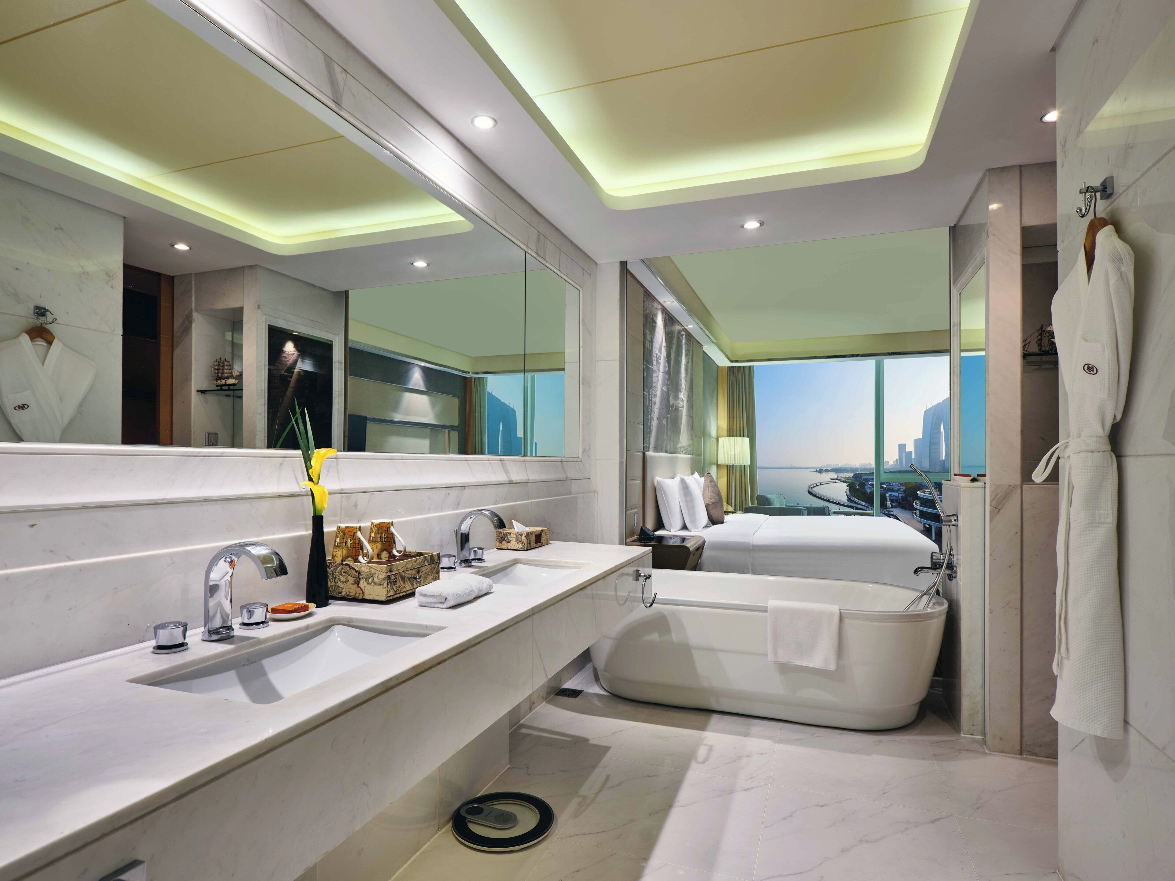 Een moderne badkamer met een grote spiegel, twee wastafels, een bad en uitzicht op een stadsgezicht.