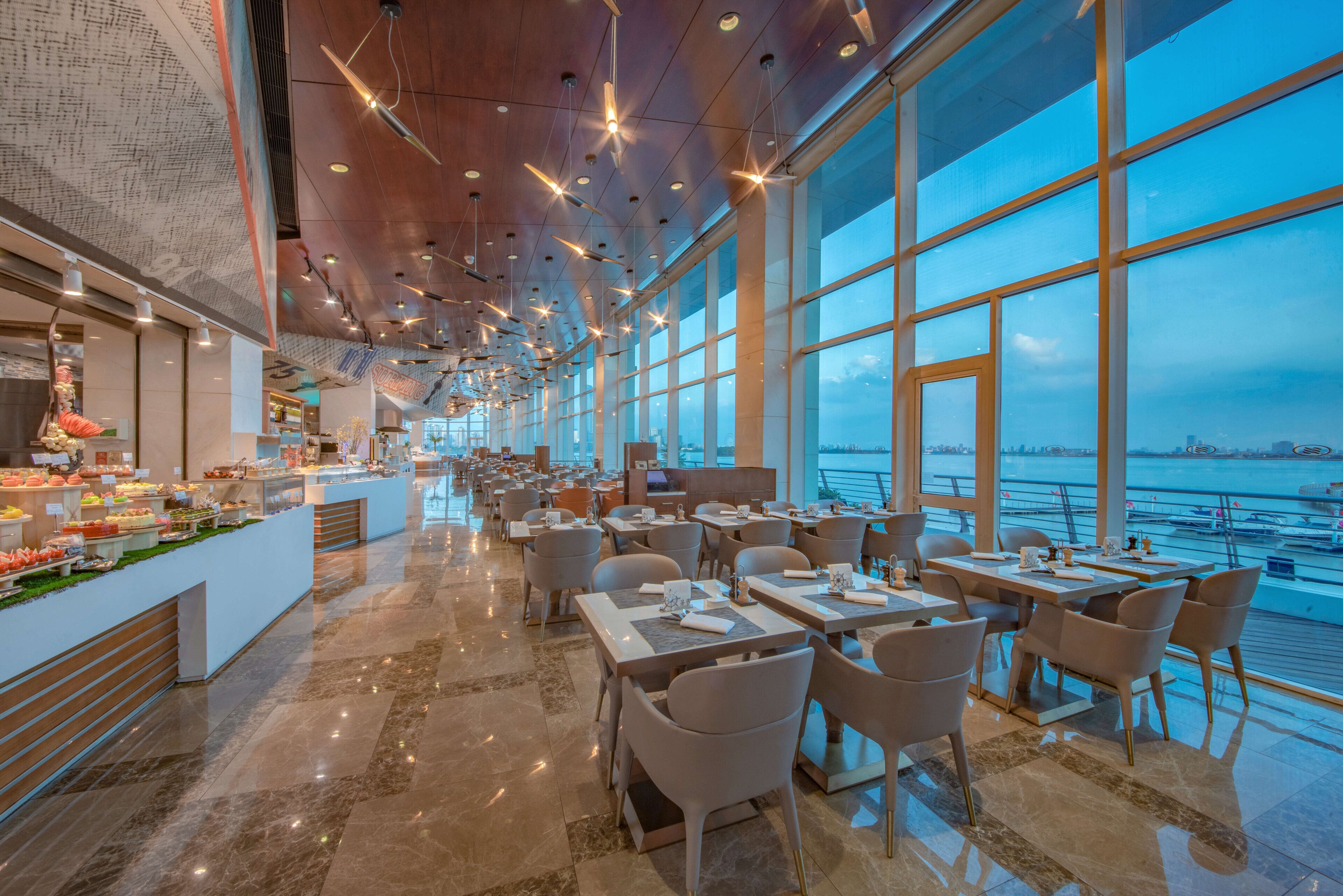 A spacious restaurant with a long counter, multiple tables, and a view of the water.
