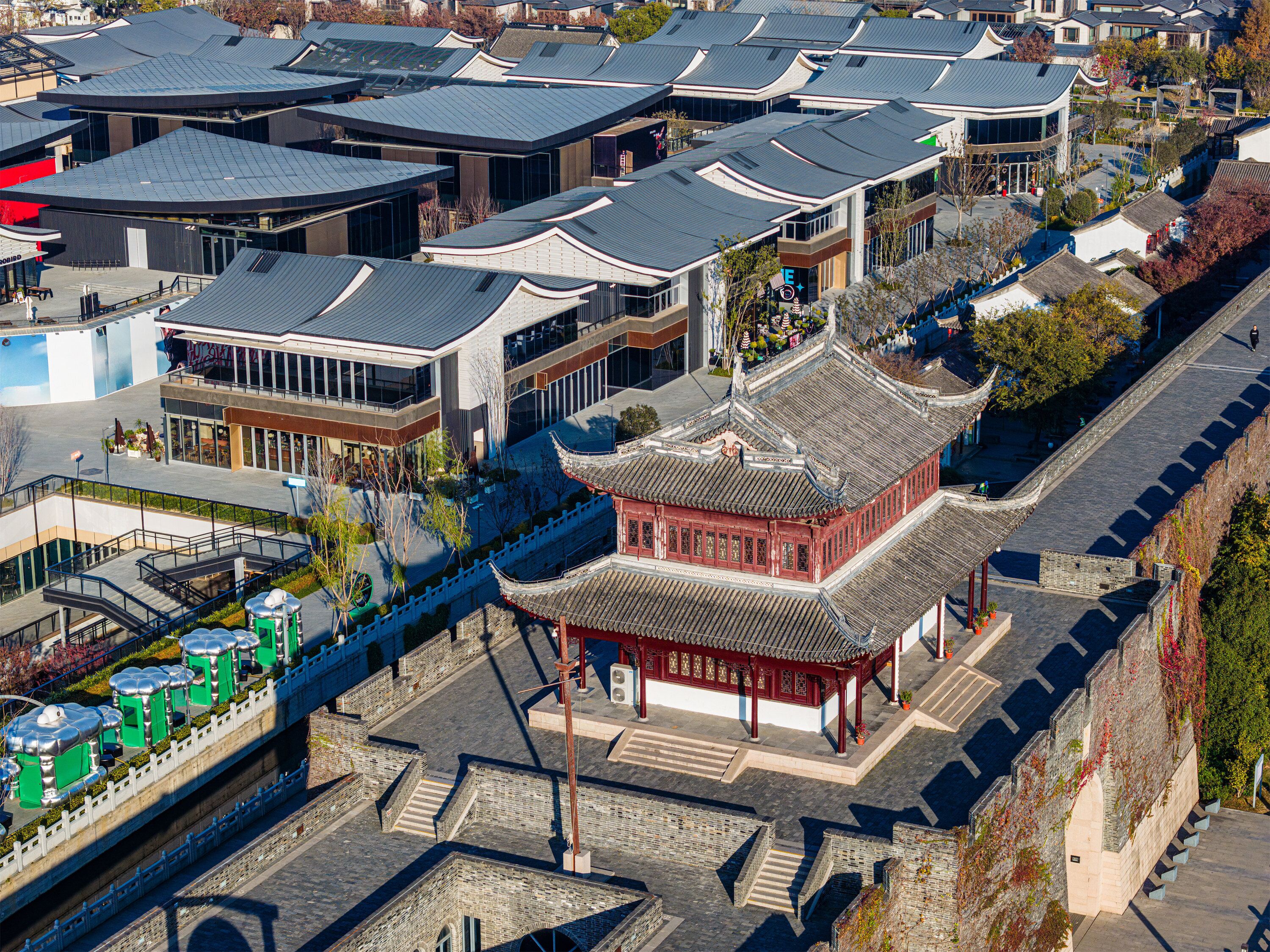 A traditional Chinese building with a red roof and white walls, surrounded by modern buildings with grey roofs.