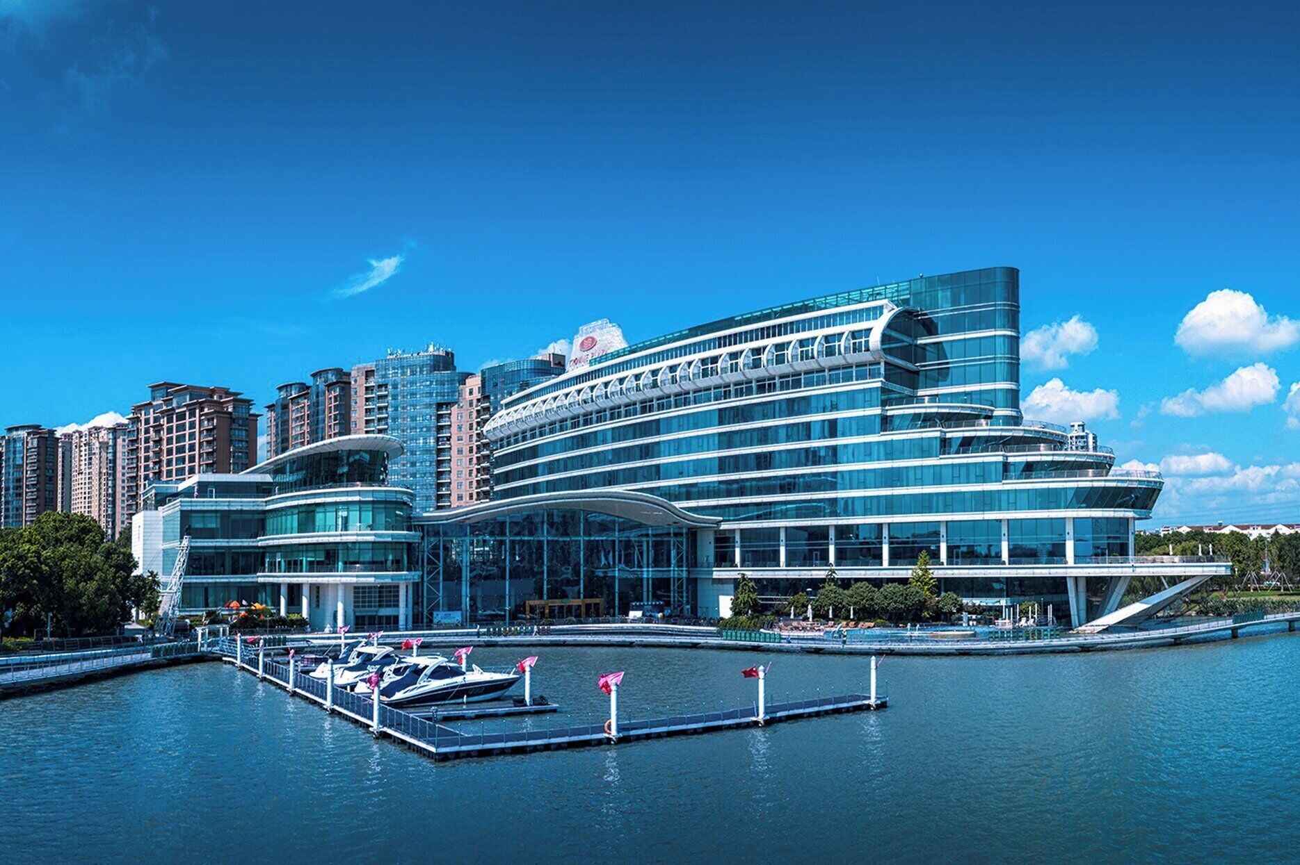 A modern hotel with a waterfront view, featuring a glass facade and a dock with boats.