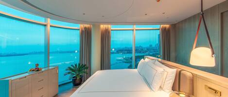 Habitación de hotel moderna con una cama grande, vistas de la ciudad y un balcón con panorama urbano.