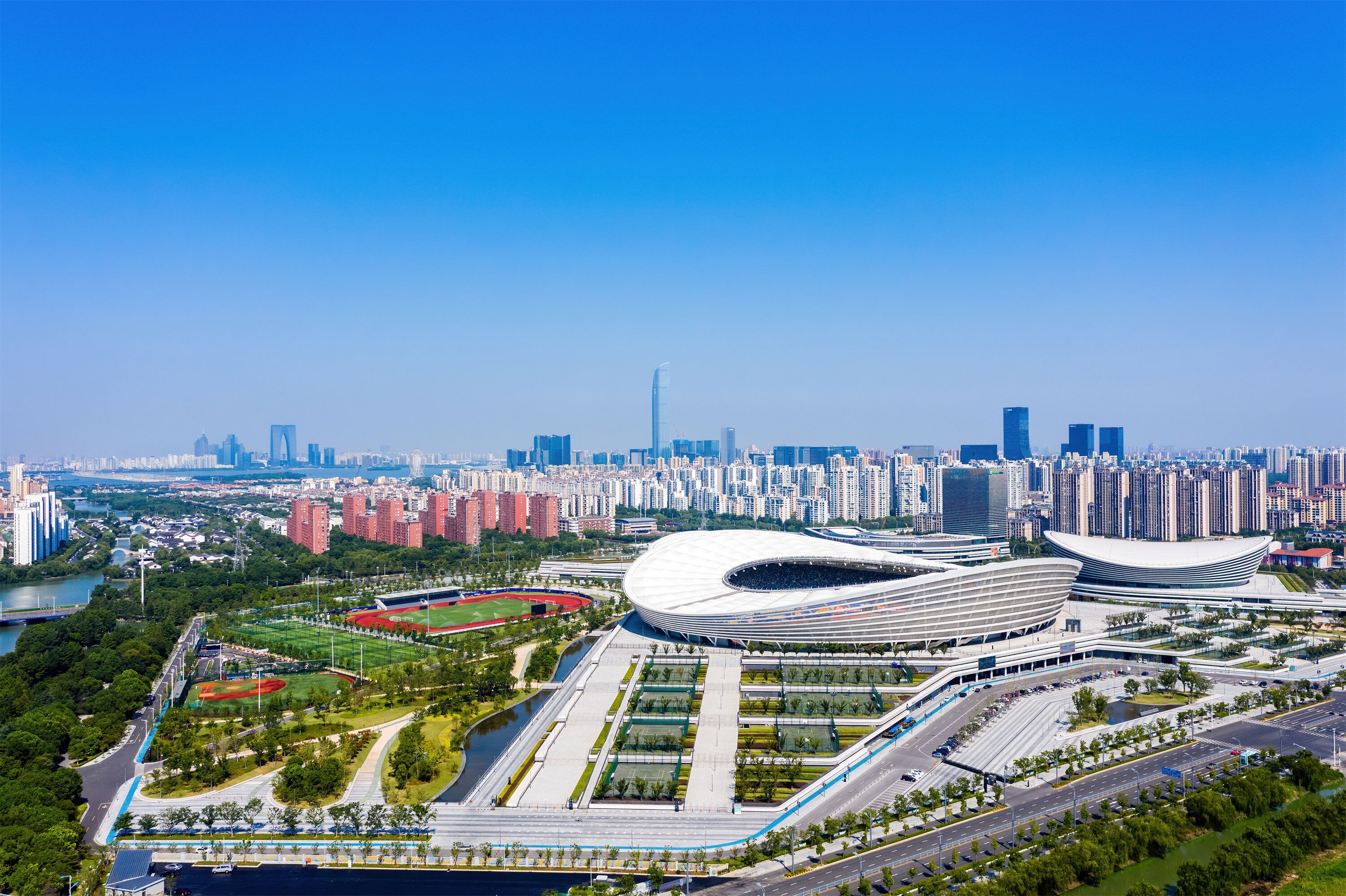 Uno stadio moderno con un tetto dalla forma originale, circondato da un parco curato e da un fiume.