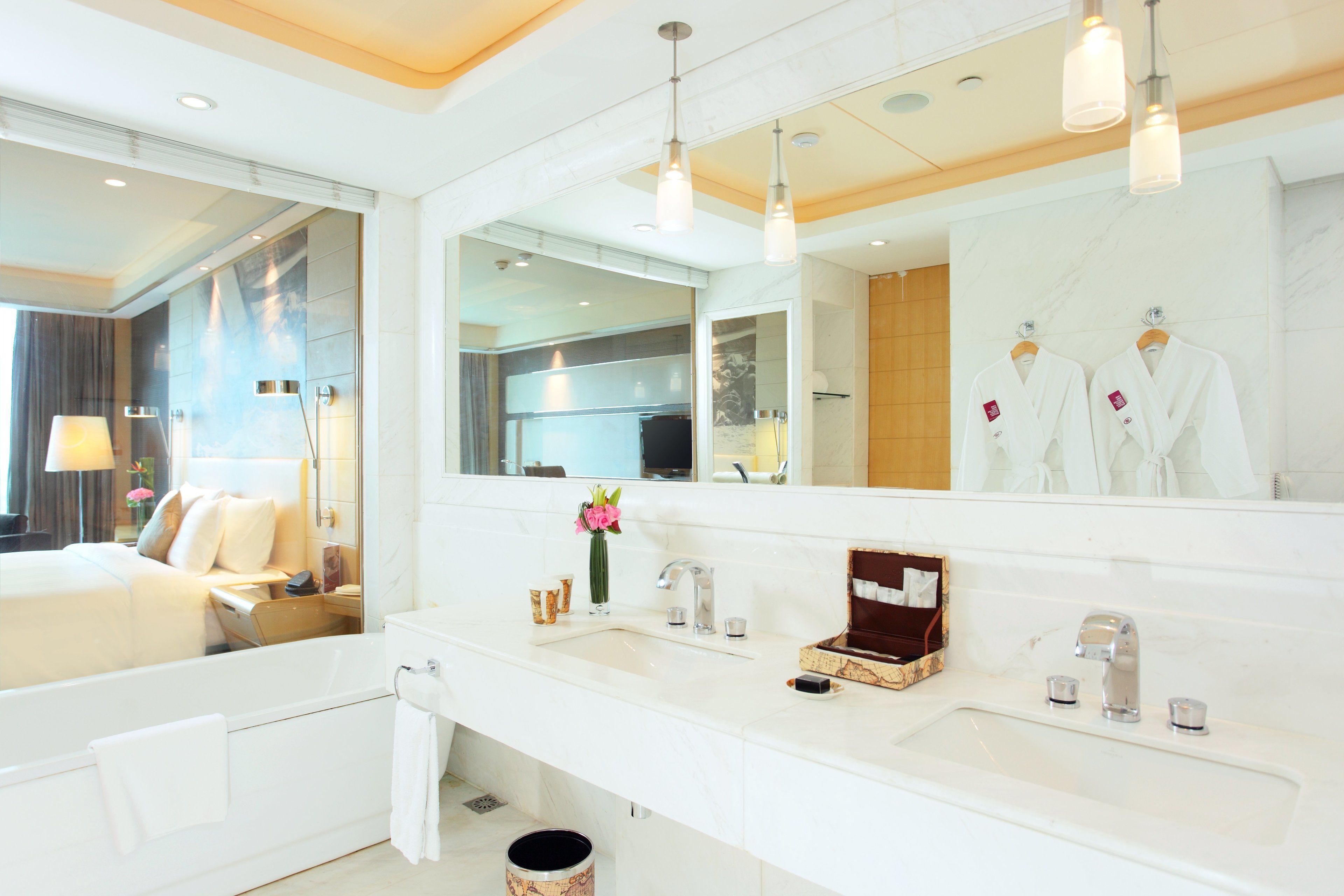 A modern hotel bathroom with a large mirror, white countertops, a bathtub, and a vanity with a sink and towel rack.