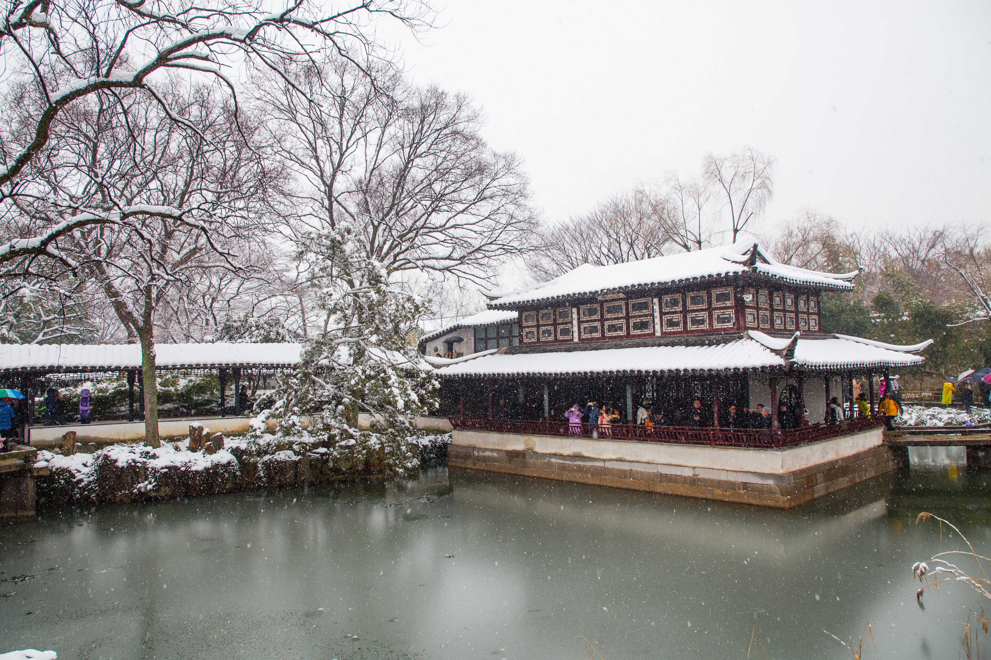 A traditional building with a snow-covered roof and a pond in front.