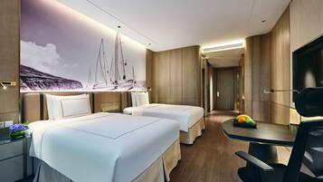 A hotel room with two beds, a desk, a chair, a TV, and a mural of sailboats on the wall.