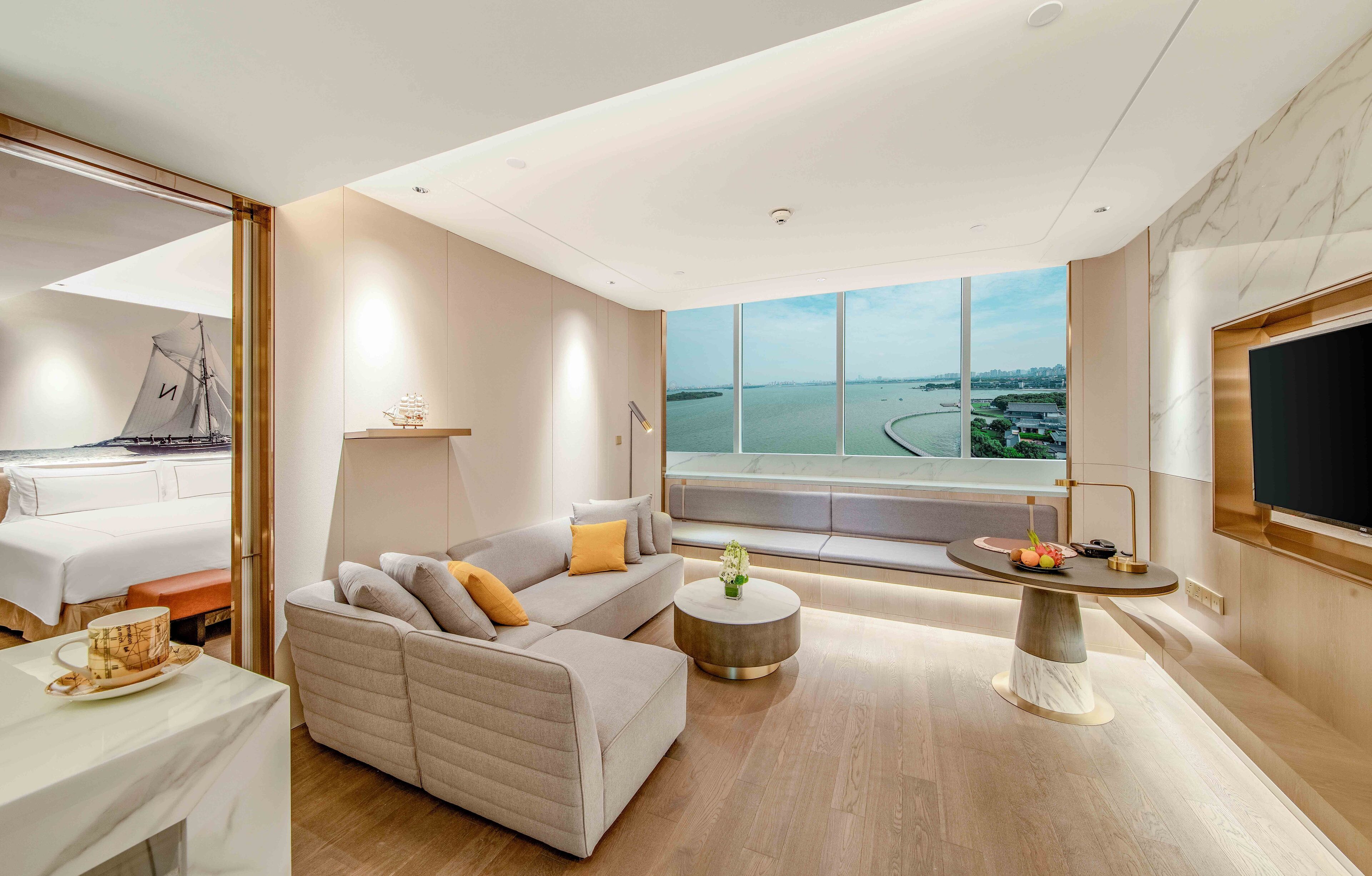 Une chambre d’hôtel moderne avec un grand lit, un canapé, une table basse ronde et un téléviseur.