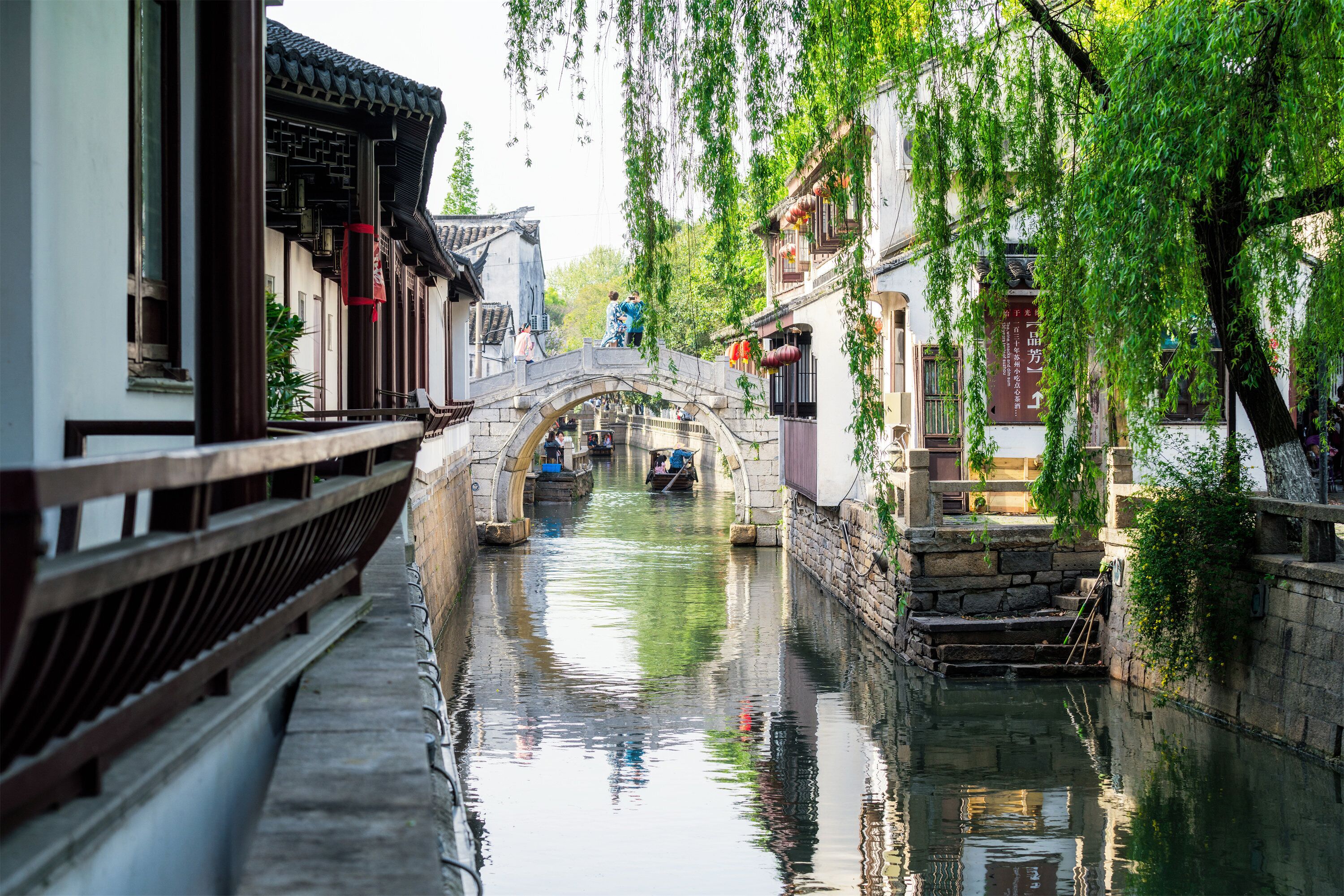 A traditional Chinese courtyard with a stone bridge, narrow waterway, and traditional buildings.