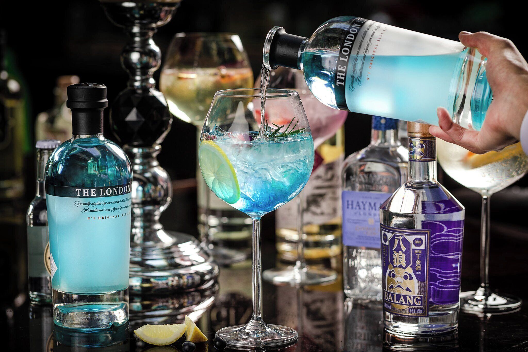 A bar setting with a hand pouring a blue liquid into a glass.