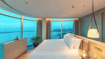 A modern hotel room with a large bed, a view of the city, and a balcony with a plant.