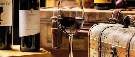 A glass of red wine on a wooden surface with vintage trunks and bottles in the background.