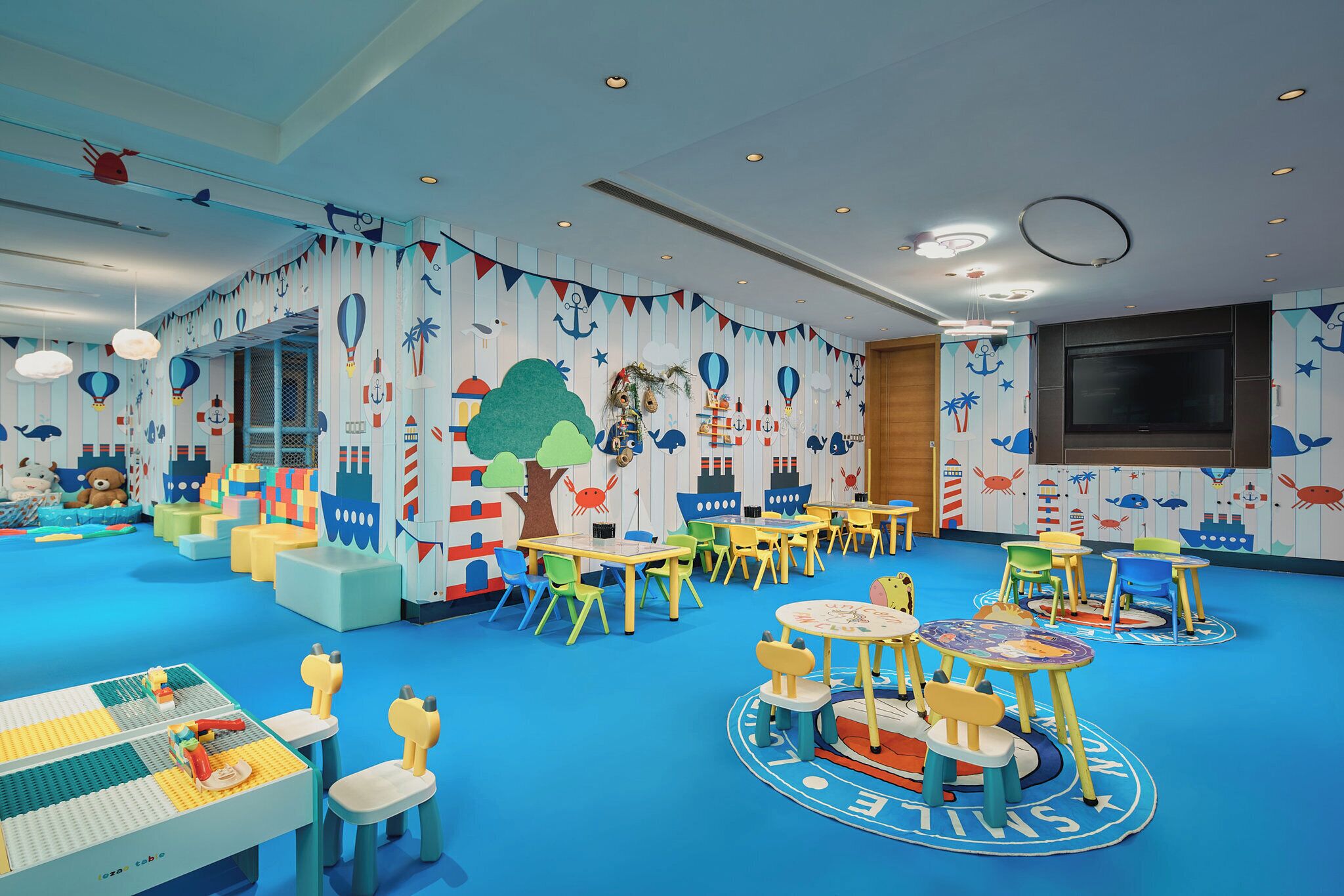 Un cuarto de juegos infantil con mobiliario colorido, paredes con motivos náuticos y suelo azul.